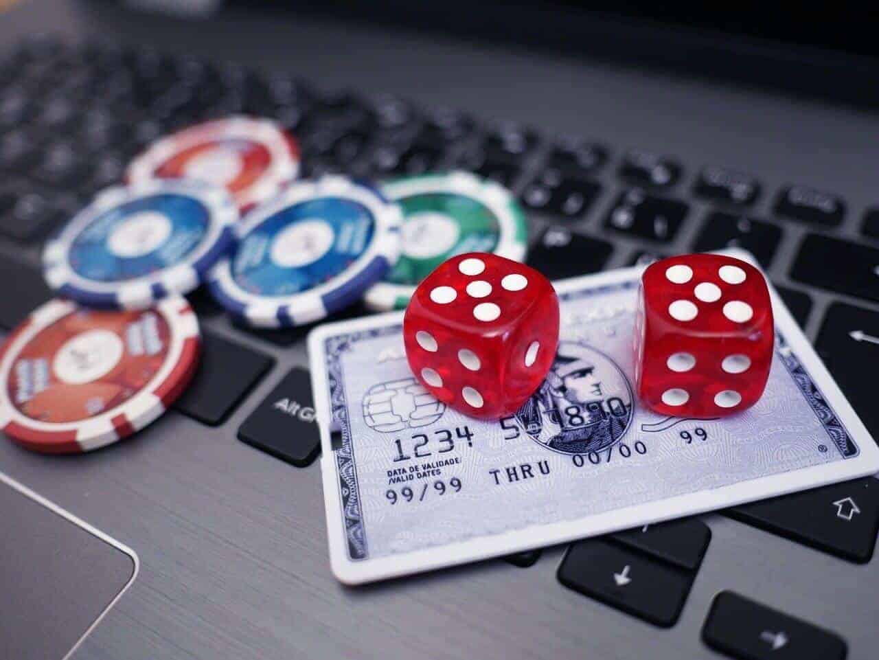 ลูกเต๋าสีแดงและชิปคาสิโนบนแล็ปท็อปพร้อมบัตรธนาคาร
